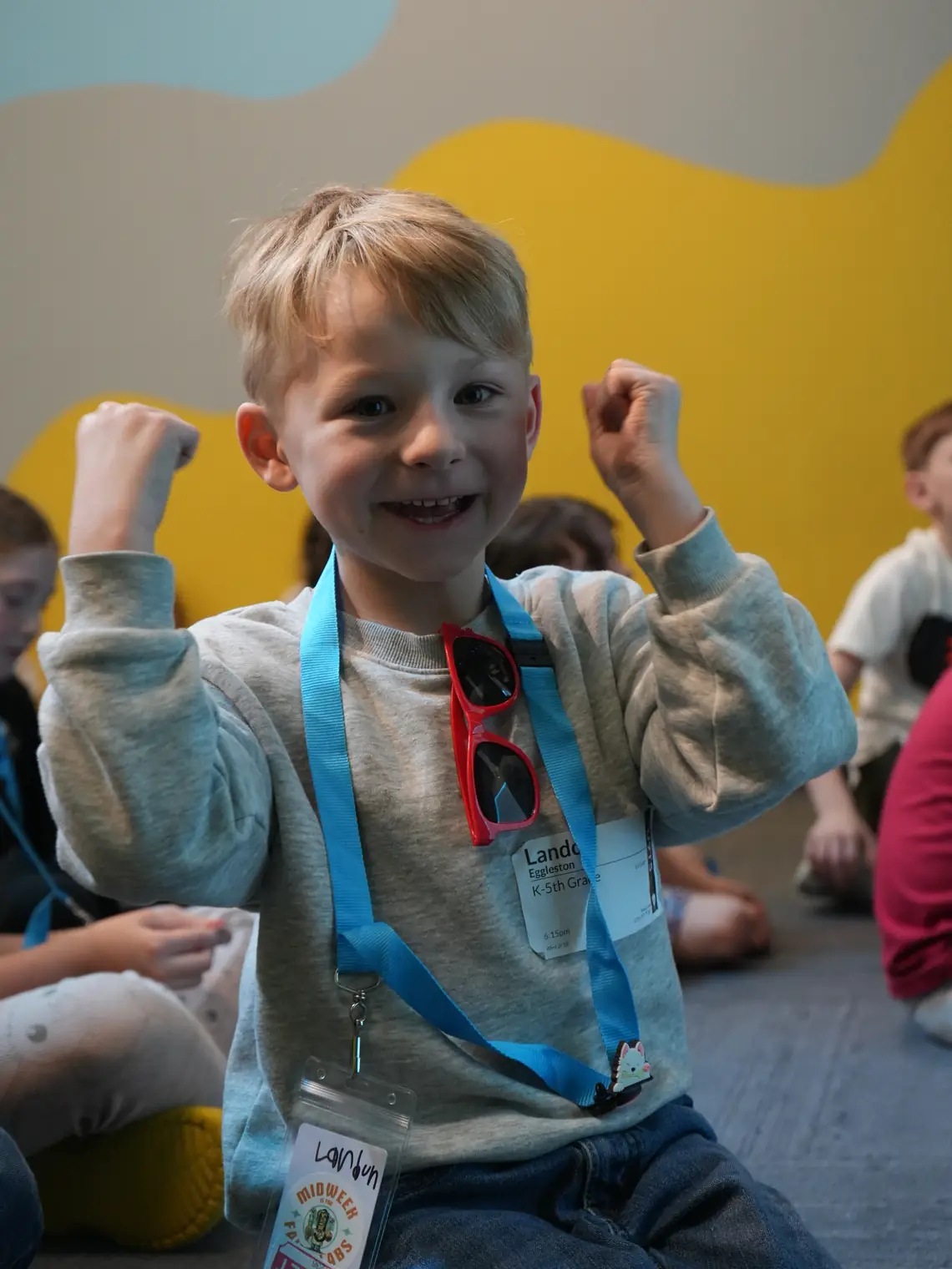 A boy wearing a Faith Labs name tag punching both fists in the air, grinning.