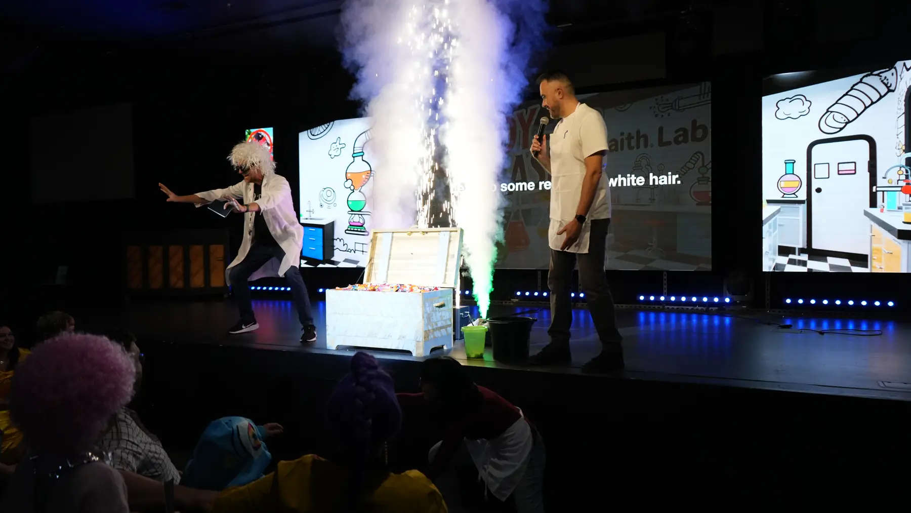 A spark fountain erupting from a crate on stage while kids in costume watch from the floor.